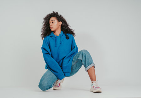 A beautiful curly-haired girl posing in a blue sweater and jeans on a white background
