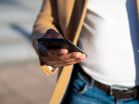 A closeup of an African male using his phone outdoors with a blurry background