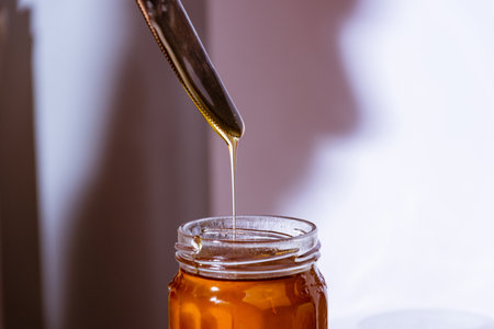 A closeup shot of a person taking honey out of a jar with a knife