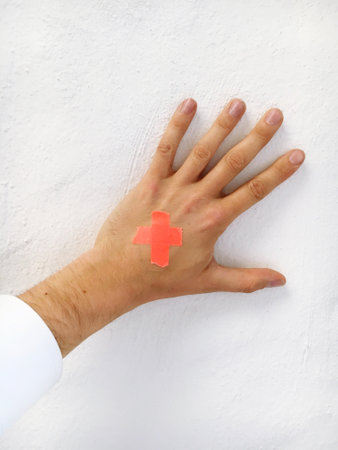 A vertical shot of a hand on a white background with a cross made of orange bandaidsの写真素材