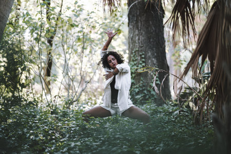 A young caucasian curly female posing in the forest with expressive movementsの写真素材