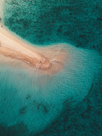 An aerial shot of the ocean waves hitting the small sandy islandの写真素材