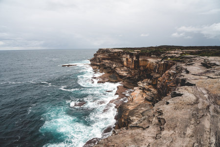 A beautiful shot of a large cliff next to blue water on a gloomy dayの写真素材
