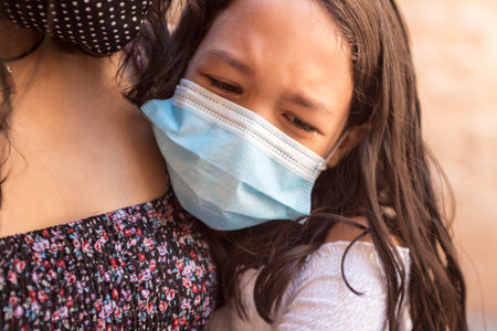 A closeup shot of a little girl in tears wearing a facial mask during the CV19 pandemic - concept of new normalの写真素材