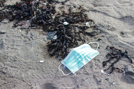 A closeup shot of a medical mask on a beach - Coronavirus waste polluting nature conceptの写真素材