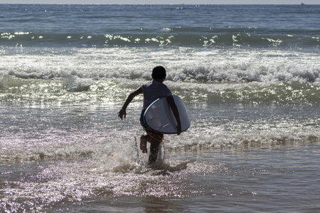 A closeup shot of a kid running to the sea with a surfing board