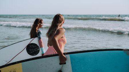 Two female surfers holding their surfboards and walking to the seaの写真素材