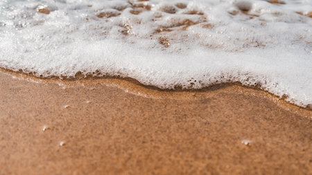 A high angle shot of the foamy waves coming towards the sandy beachの写真素材