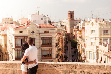A back view of a young tourist couple looking out at buildings in a cityの写真素材