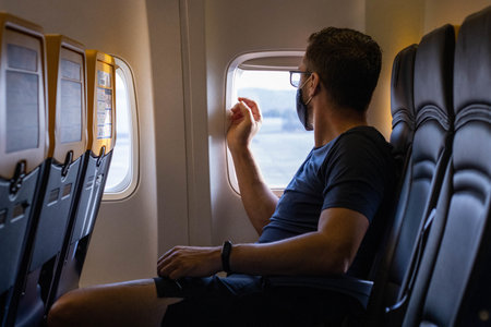 A young Caucasian male traveling on the plane with a medical mask - the new normal after Covid-19の写真素材