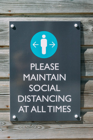 A vertical shot of a wall sign with text Please Maintain Social Distancing at All Timesの写真素材