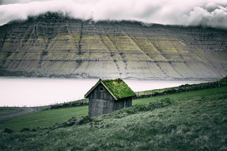 A horizontal view of a brown wooden shed with grass on the roof on a background of rock cliffsの写真素材
