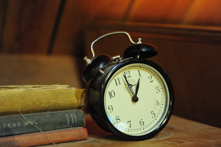 A closeup shot of a vintage alarm clock next to a dusty pile of books
