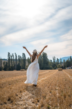 A vertical shot of a cheerful female in a white dress running through a field under the sunlightの写真素材