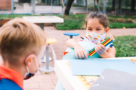 Children wearing face masks draw pictures with colored pencils when they leave school after the...