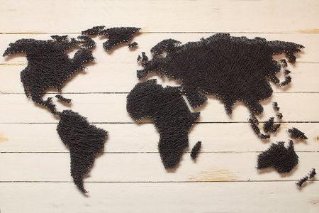 A closeup of a small map of the world made with nails and threads on a wooden surfaceの写真素材