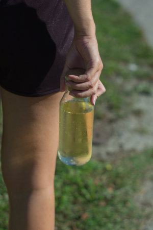 A vertical closeup shot of a hand holding a clear bottle of yellow liquidの写真素材