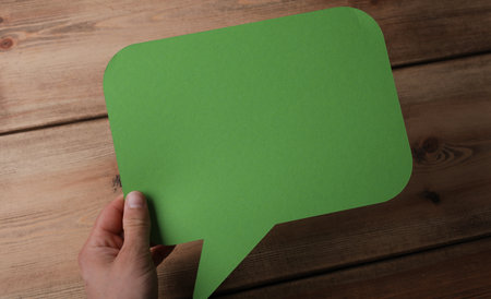 A closeup shot of a man holding a green message icon on a wooden backgroundの写真素材