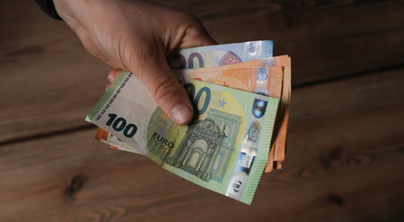 The hands of a man holding European Euro bills with the wooden table in the background
