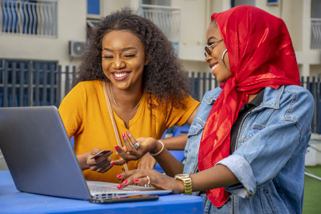 A closeup shot of two cheerful young African ladies and a laptopの写真素材