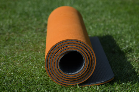 A closeup of an orange yoga mat on the grass under the sunlightの写真素材