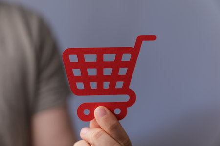 A closeup shot of a man holding a red shopping cart icon on a grey backgroundの写真素材