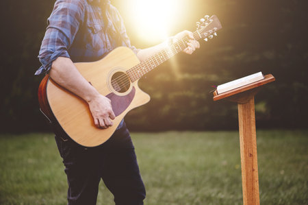 A man holding a guitar and standing on a green lawnの写真素材