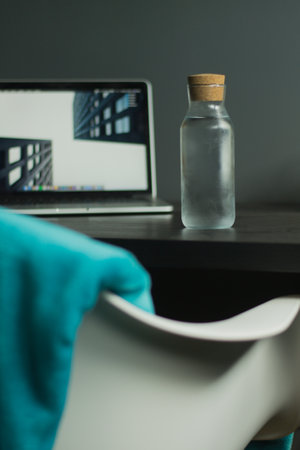 modern glass bottle filled with water sitting on desk with other thingsの写真素材
