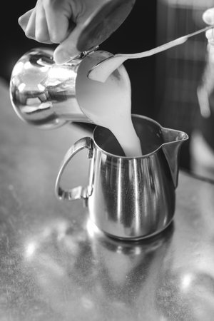A grayscale shot of a female barista at work preparing milk for espresso coffee macchiato or cappuccino in a barの写真素材