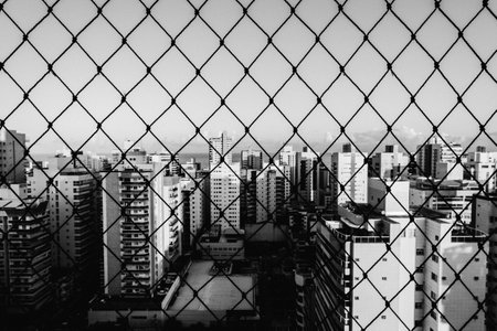 A grayscale shot of a district behind a chain-link face