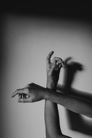 A grayscale vertical shot of graceful hands with a shadow on a wallの写真素材