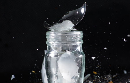 A closeup shot of small glass jar with broken pieces on dark backgroundの写真素材