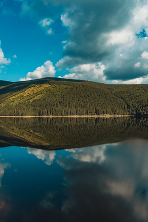 A vertical shot of the reflection of a hill and the beautiful sky in the calm lakeの写真素材
