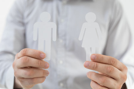 A closeup shot of a male holding two people figurine paper cut-outs under the lightsの写真素材