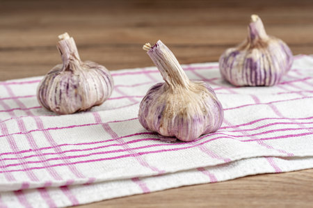 A selective focus shot of heads of garlic on a towel on the wooden tableの写真素材