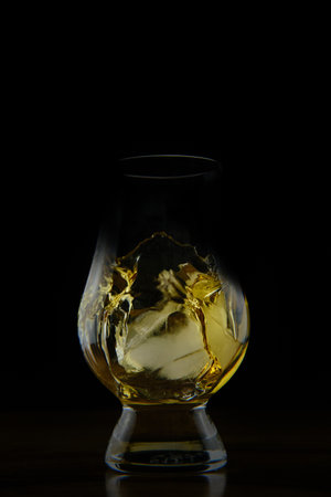 A vertical shot of a splashing golden coloured liquid in a glass isolated on a black backgroundの写真素材