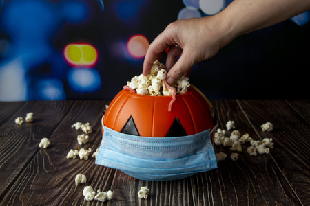 A closeup shot of a Halloween pumpkin with popcorn and a sanitary mask-concept of the new normalの写真素材