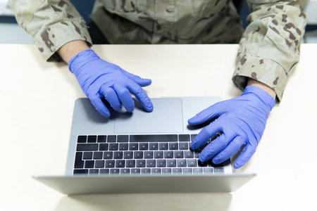 A closeup shot of uniformed military male with medical gloves using his laptopの写真素材