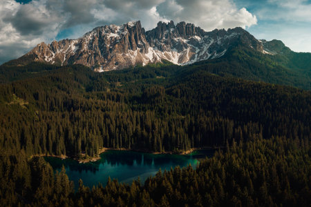 The Karersee surrounded by forests and Dolomites under a cloudy sky in Italy
