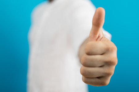 A closeup of a person doing the thumbs-up gesture under the lights on a blurry background