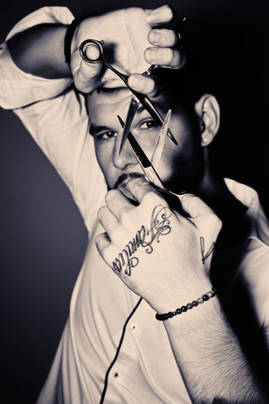 A vertical grayscale shot of a young barber holding scissors in front of his face