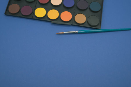A closeup shot of a watercolor palette and a brush isolated on a blue backgroundの写真素材