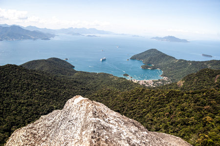 A beautiful shot of a seashore with forested mountains in Pico de Papagayo, Ilha Grande, Brazilの写真素材