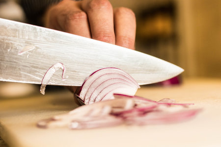 A closeup shot of a person slicing a red onion with a knifeの写真素材