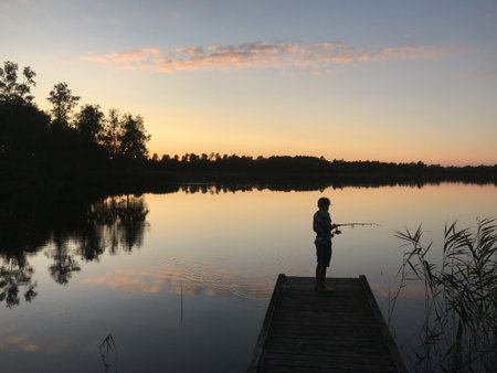 A person fishing from the lake surrounded by treesの写真素材