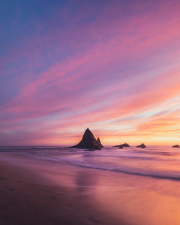 A beautiful scenery of a rocky cliff in the sea with the breathtaking view of sunsetの写真素材