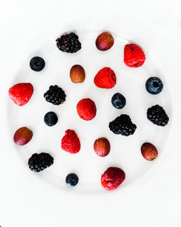A top view of carious berries artfully arranged on a white plate