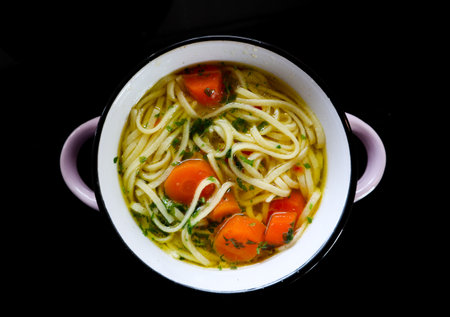 A high angle shot of a pot of noodles and vegetables on a black surfaceの写真素材