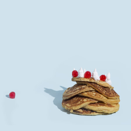 A closeup shot of a stack of pancakes with whipped cream and candy on a blue surfaceの写真素材