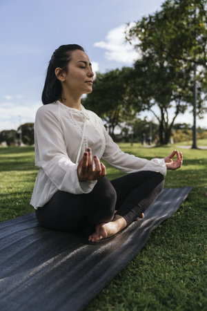 A vertical shot of a Hispanic female doing yoga at a parkの写真素材